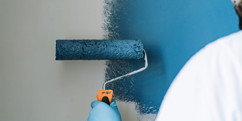 caucasian bearded man painting wall with paint roller. Painting apartment, renovating home with blue color paint. Image with selective focus
