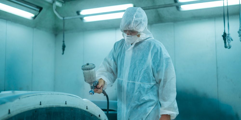 Caucasian man is using painting gun in repair shop